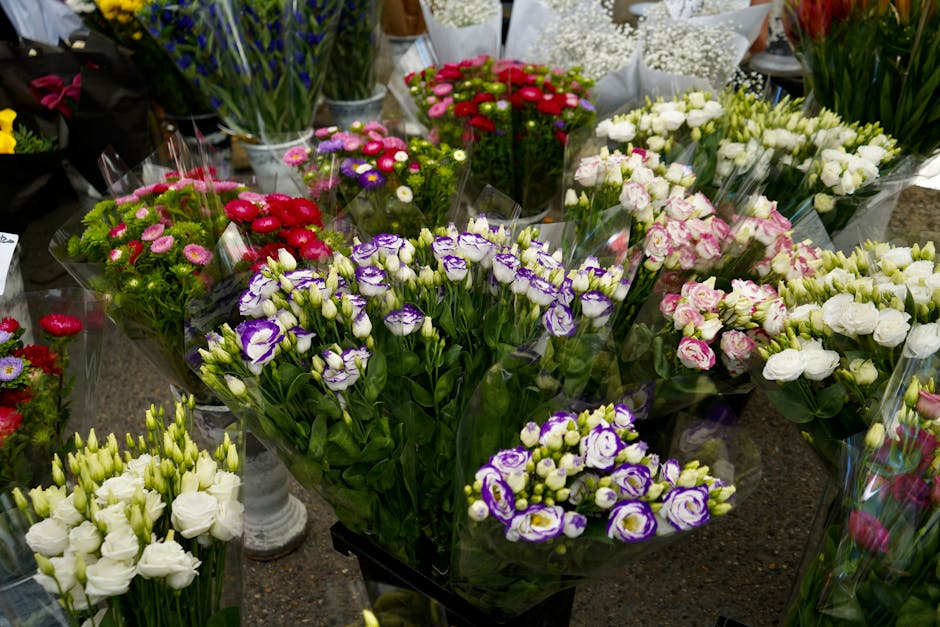 A vibrant display of fresh florist flowers arranged in bouquets and wrapped in clear cellophane, including purple and white irises with delicate petals, clusters of small pink and red blooms, and whit