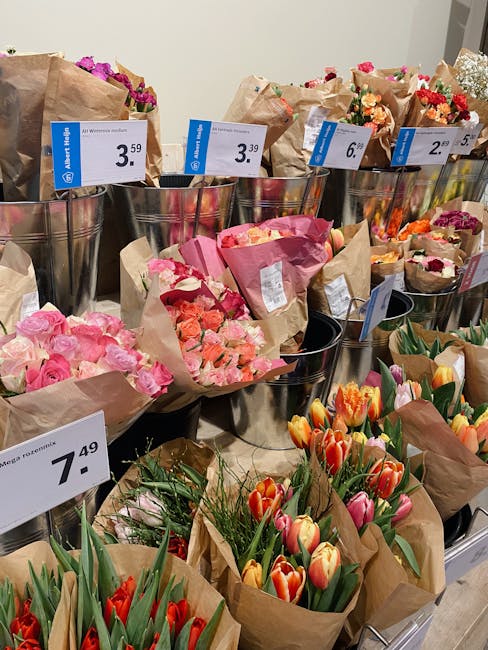 A display of various floral arrangements and bouquets at Hackney Marshes Florist, arranged in metal buckets and wrapped in brown craft paper. The flowers include pink roses, orange and pink tulips, an
